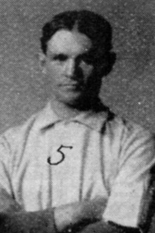 A man in a white baseball uniform with his arms crossed.