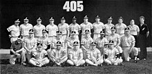 A black and white photograph of baseball players in uniforms and caps posed in three rows standing, sitting, and kneeing on a baseball field