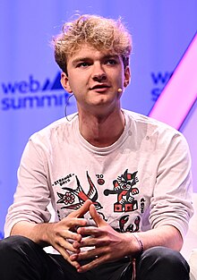 Casually dressed young man with curly hair talking while sitting on a chair