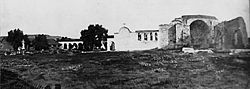 An overall view of the "Mission of the Swallow" around the time of Father St. John O'Sullivan's arrival in 1910. The Mission's once-renowned California pepper tree can be seen just to the left of the adobe church's espadaña.