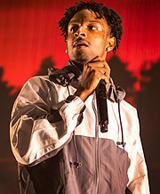 21 Savage holds a microphone and looks to his right