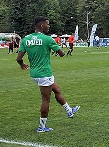 A player standing up lift his left leg above the ground during warm-up