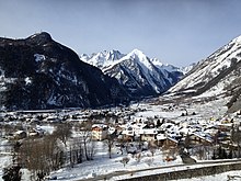 Snow covered village in valley with snow capped mountains in background taken from an elevated position on a walking trail though hills and forests