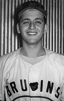 A man smiles for the camera in a baseball cap and jersey with "Bruins" written across the chest.