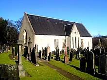 An image of an old, cream coloured church building. In the foreground are an array of gravestones and memorials.