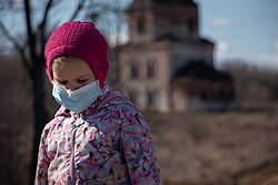 Young girl looking down, wearing a with a pink beanie, floral puffer and a surgical mask