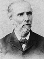 Photo shows a gray-bearded man in a black civilian suit.