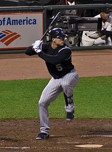 A man in a black baseball jersey and gray pinstriped pants prepares for a right-handed baseball swing.