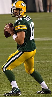 Aaron Rodgers in a Green Bay Packers uniform and helmet with a football in his hands preparing to pass.