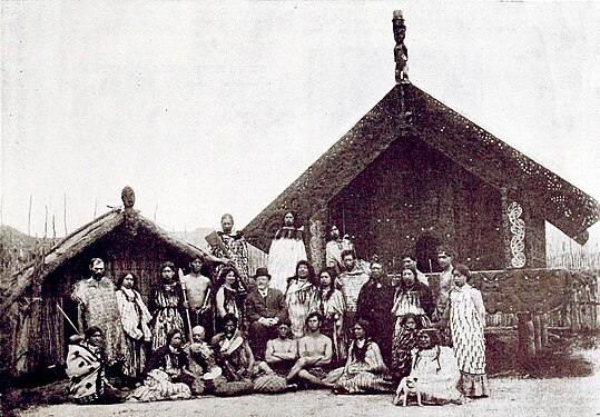 Posed photo of a group in front of a traditional Maori house.