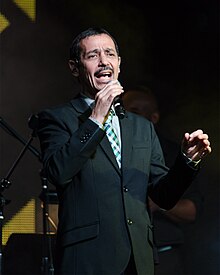 A man is facing the camera while holding a microphone with his right hand.