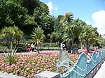 blue railings in front of a park with colourful flower beds and palm trees