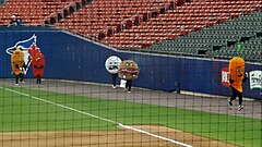 People in food costumes racing around the warning track at a ballpark