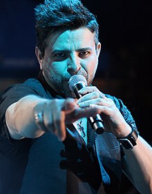 Man holding a microphone is pointing towards the camera.