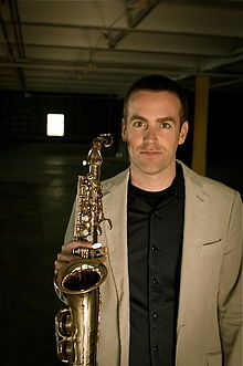 white male holding saxophone, looking directly into the camera