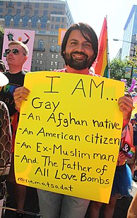 Nemat Sadat holding a handmade poster which says, "I am... gay, an Afghan native, an American citizen, an Ex-Muslim man, and the Father of All Love Bombs"