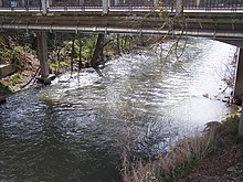 A large stream about 15 feet (4.5 m) across, spanned by a concrete bridge (not Antelope Creek Bridge) with metal pipes underneath it. Sparse vegetation grows along the creek's banks.