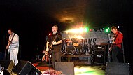 Four men on a stage playing instruments and singing into microphones