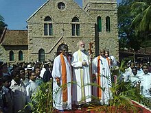Archbishop of Canterbury visiting the church in 2010 standing in between two local priests surrounded by a large crowd