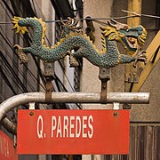 A red street sign that says "Q. PAREDES" The street sign is topped with a dragon.