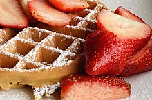 Round waffle topped with strawberries and powdered sugar