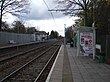 A set of two railway tracks between two platforms with shelters. There is a mesh fence between the two tracks.