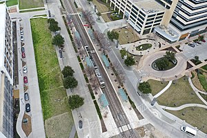 An aerial view of a double-tracked rail line surrounded by two side platforms. The CityLine development is visible to the right.