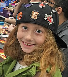 Head and shoulders of Fischer, an eight-year old girl with reddish blonde hair in a black baseball cap and green costume
