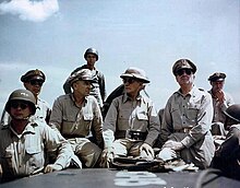 Eight men in khaki uniforms, seated.