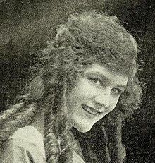 Young white woman with long cylindrical curls, smiling, 3/4 profile.