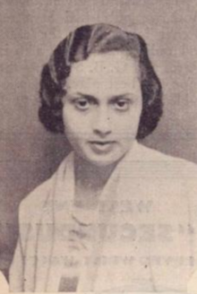 A young South Asian woman with fair skin, dark hair in marcelled waves, wearing a light-colored soft garment