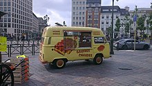 Sitting in a city square is a yellow van decorated with images of waffles and with serving window on the side