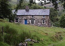 A colour photograph of a stone cottage on a hill