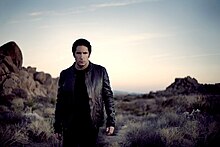 A man dressed in black walking through a desert at sunset.