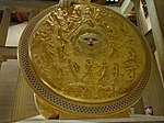 Bouclier doré et décoré d'une scène de bataille, un visage au centre