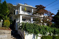 Photograph of a house sitting up a short, steep slope above the street.