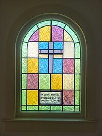 a colorful glass window with a subdued cross in it and the text "in loving memory Rev. William T. Collins Jan. 1901-Apr. 1951"