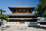 Large wooden building with a hip-and-gable roof, two enclosing pent roofs and an open gallery with handrail on the upper floor.