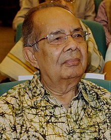 Color photograph of Dutta seated in a chair wearing glasses and a light green shirt.