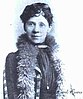 Photograph of a woman with short black hair, wearing a feather boa around her neck