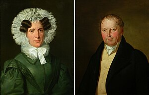 At left, a painted portrait of a woman in a black dress with a frilled hood and ruffled collar. At right, a painted picture of a man in a black coat wearing a cravat.