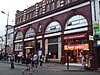 A red-bricked building with a blue sign reading "CAMDEN TOWN STATION" in white letters and a red sign reading "FIRST CHOICE RESTAURANT" in white letters