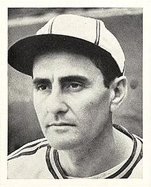 A man in a white baseball jersey and cap with dark stripes looksto the left.