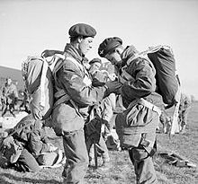 Two men in the foreground check each other's equipment, mere men are in the background