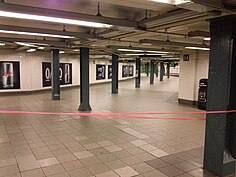 View of a corridor sloping upward from the IRT mezzanine to the BMT mezzanine. The corridor is wide and contains tiled floors, a low ceiling, and green columns.