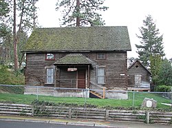 Photograph of the Anderson house and granary, a rustic, two-story, wooden house, with a smaller auxiliary building behind, also rustic and wooden