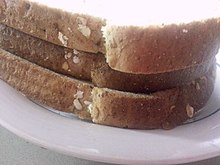 An image of a toast sandwich, shot from the side, consisting of two thin-cut slices of bread and one thick-cut slice.