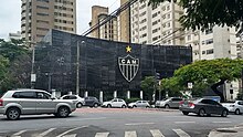 A street filled with cars in front of a metal façade in black, with a large football club badge.