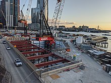 View from an elevated position of a construction site with a hole for the station box and a tower crane