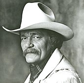 A man with a large mustache wearing a cowboy hat and light-coloured jacket